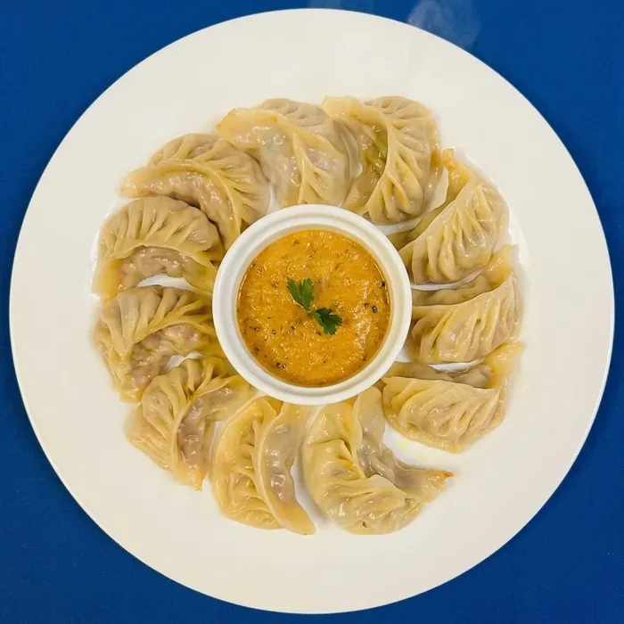 Steamed chicken momo dumplings arranged around a spiced dipping sauce
