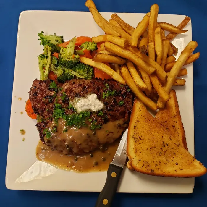 Rib eye steak with green peppercorn sauce, fries, vegetables and garlic toast