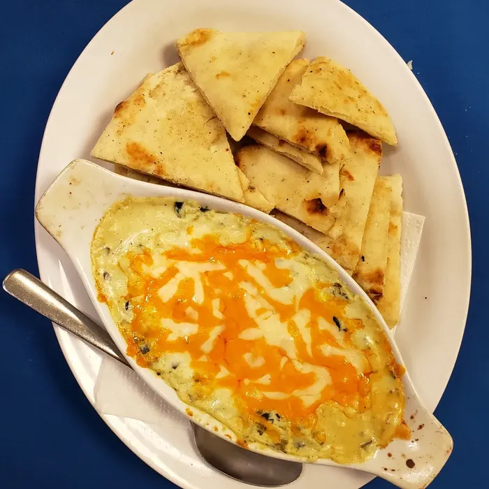 Baked spinach dip topped with melted cheese, served with warm naan bread
